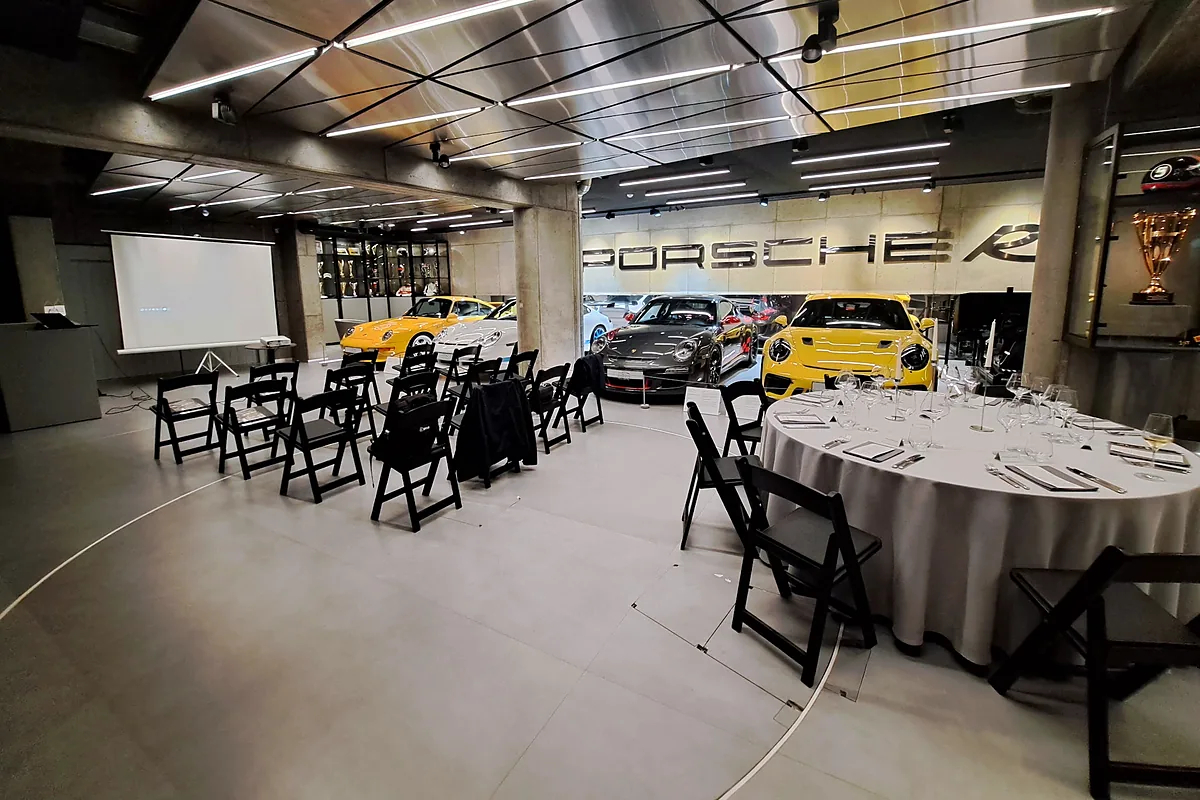 Erdvė su serviruotais stalais ir eksponuojamais Porsche automobiliais
